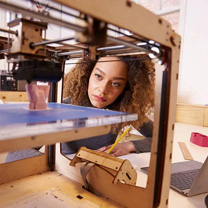 Woman observing a 3D printer creating a model, digital fabrication workspace