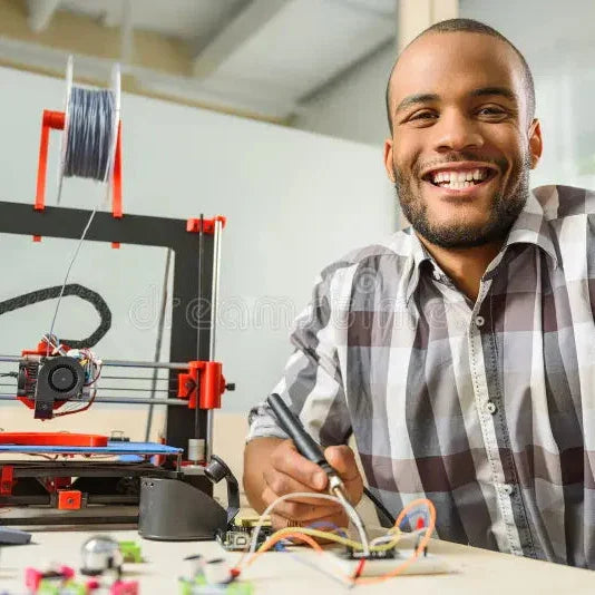 Smiling man working with 3D printer and electronics in a modern workspace