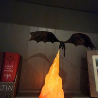 Decorative model of a dragon emerging from a book with 'A Dance with Dragons' visible, on a shelf.