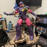 Action figure on a stand in a room with shelves and a TV.
