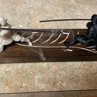 Wooden plaque with cut-out design featuring two figures and a sword on a concrete floor.